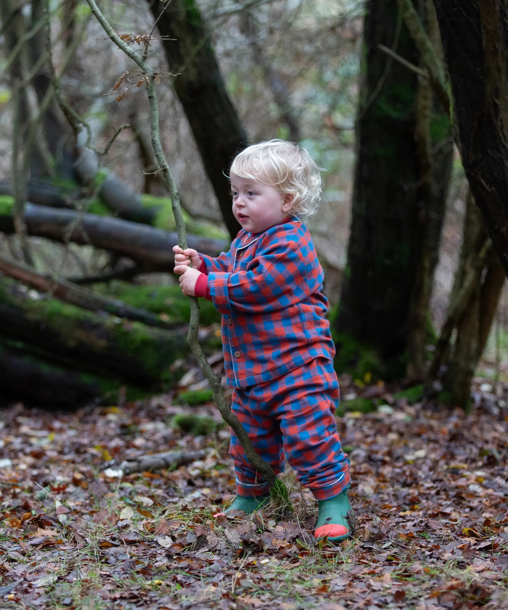 Child wearing the Little Green Radicals burnt ochre check classic pyjamas with green wellingtons.