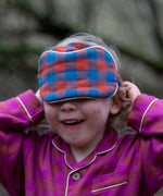 Child holding the Little Green Radicals  burnt ochre blue check organic cotton adult eye mask.