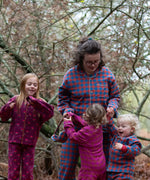 Woman wearing the Little Green Radicals burnt ochre check adult organic cotton classic pyjamas with three children also wearing Little Green Radicals pyjamas. 