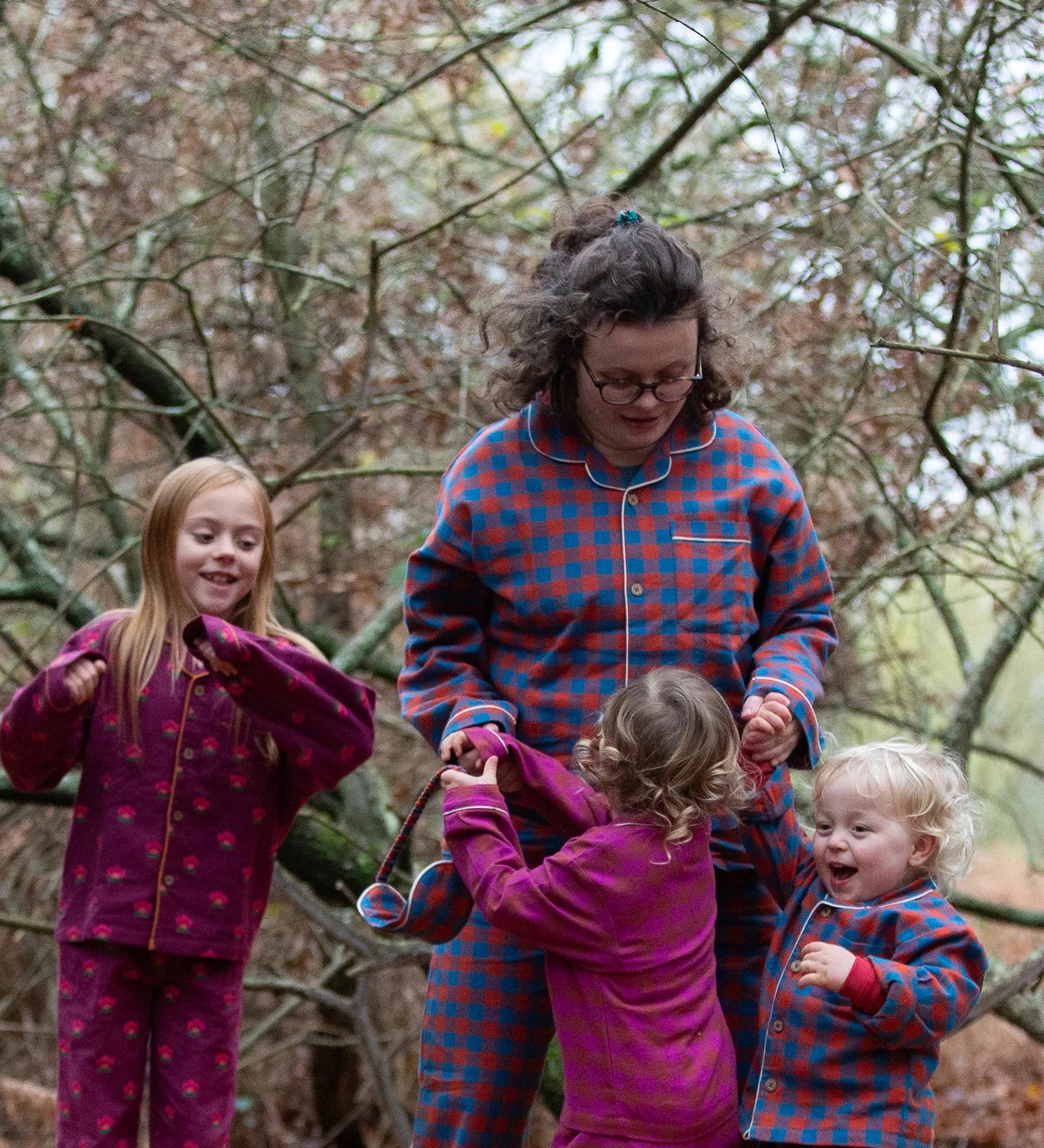 Woman wearing the Little Green Radicals burnt ochre check adult organic cotton classic pyjamas with three children also wearing Little Green Radicals pyjamas. 