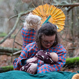 Woman wearing the Little Green Radicals burnt ochre check adult organic cotton classic pyjamas holding a baby in a all in one suit.