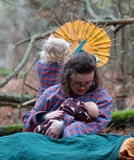 Woman wearing the Little Green Radicals burnt ochre check adult organic cotton classic pyjamas holding a baby in a all in one suit.