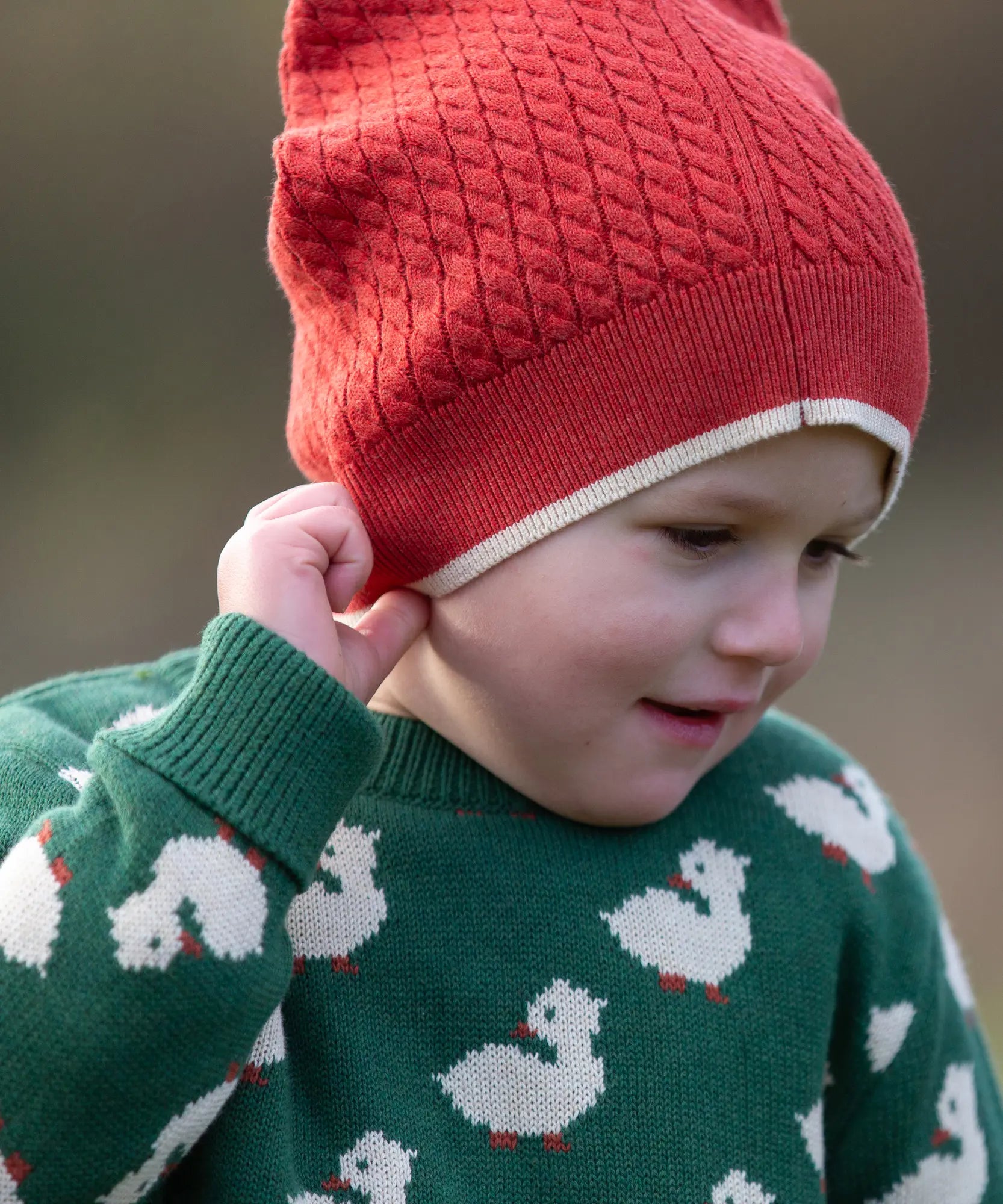 Child wearing Little Green Radicals burnt ochre knitted beanie hat with a green duck knitted jumper. 
