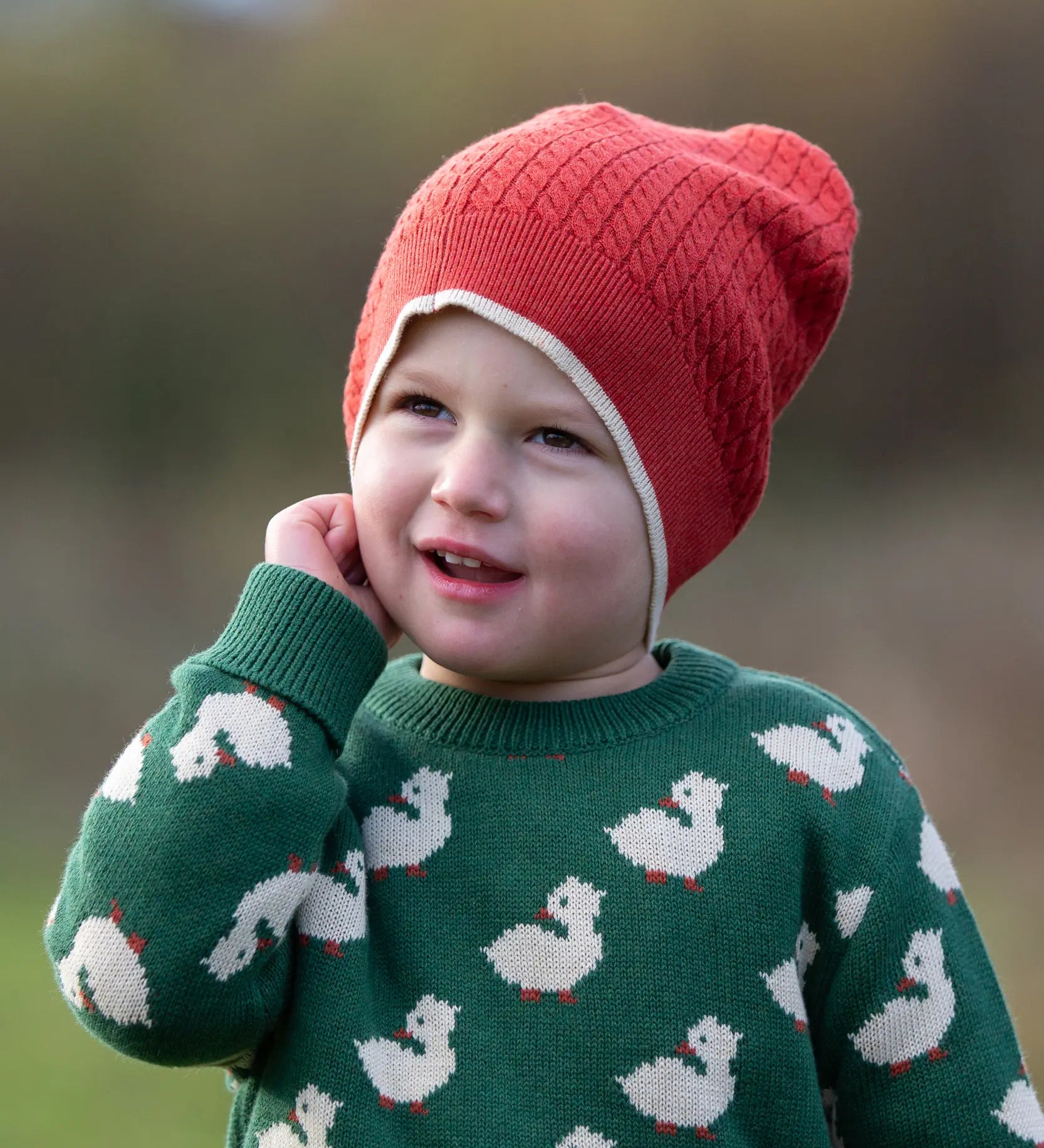 Child wearing Little Green Radicals burnt ochre knitted beanie hat with a green duck knitted jumper. 