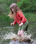 A child wearing a Little Green Radicals From One To Another Burnt Ochre Pointelle Knitted Cardigan with green coloured shorts. The child is standing in water, splashing. Little green Radicals have a wide range of organic cotton, Fairtrade children's clothing and outerwear available here at Babipur.