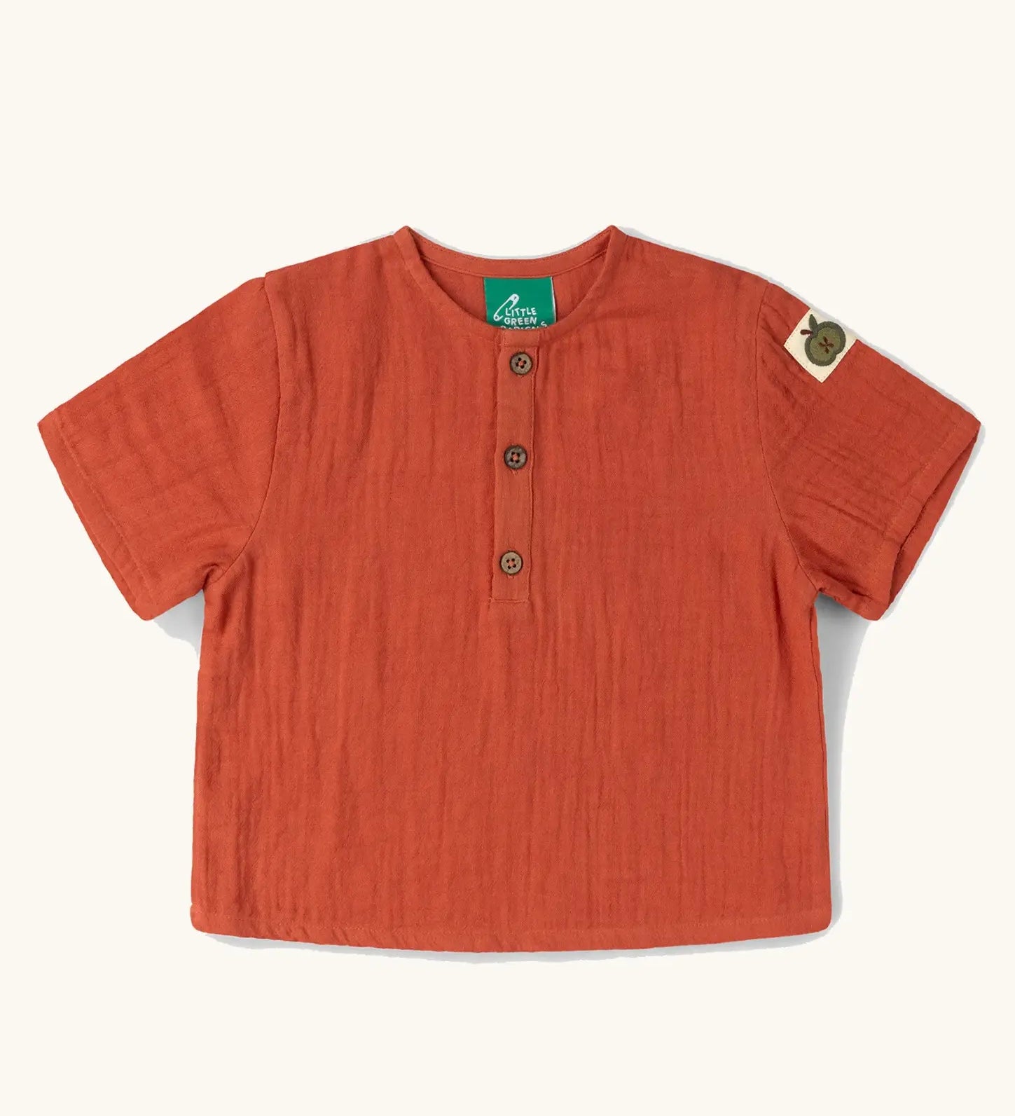 Little Green Radicals children's burnt ochre red short sleeved henley top with green apple tag on side of one arms and button up top.