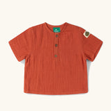 Little Green Radicals children's burnt ochre red short sleeved henley top with green apple tag on side of one arms and button up top.