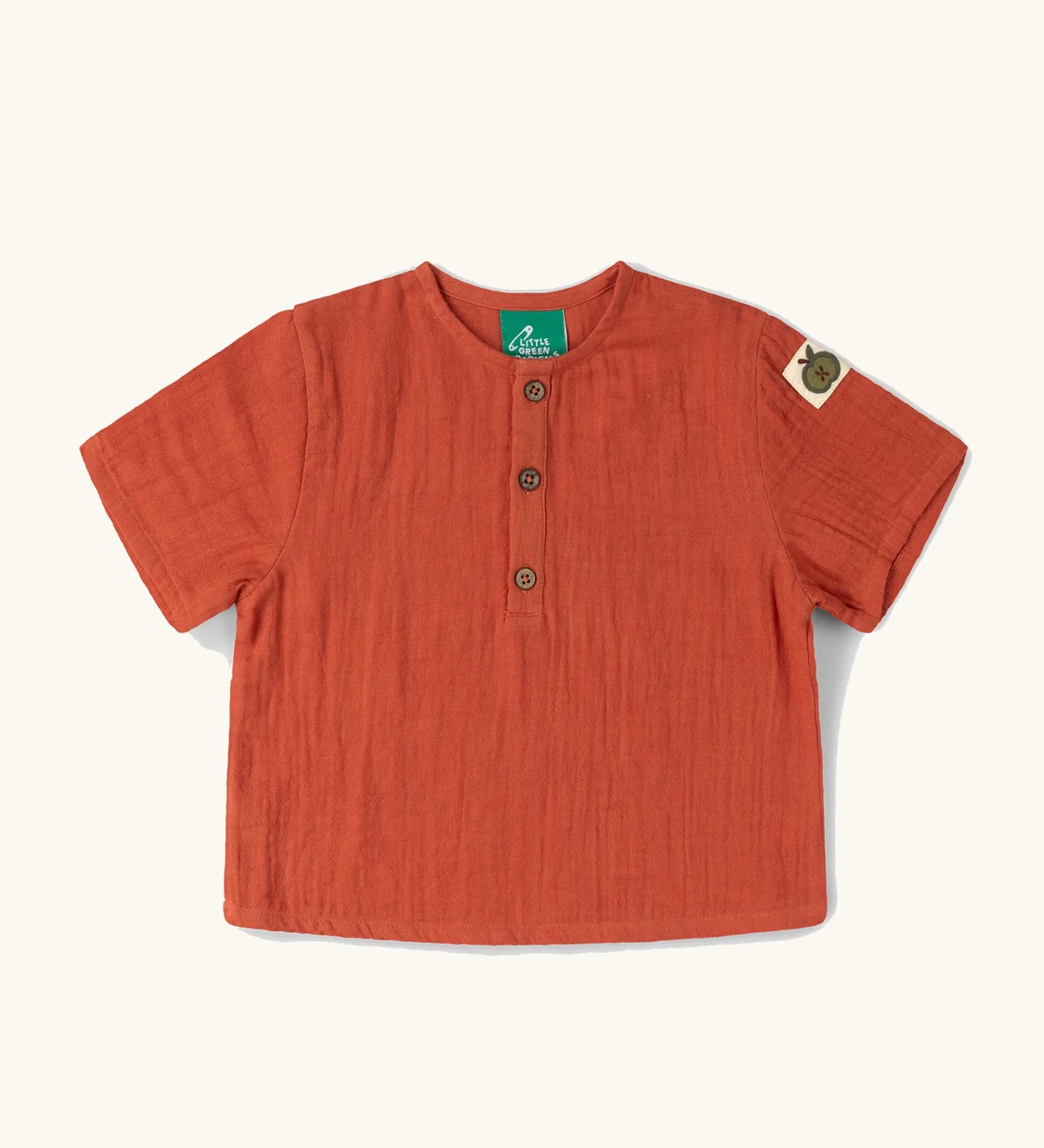 Little Green Radicals children's burnt ochre red short sleeved henley top with green apple tag on side of one arms and button up top.