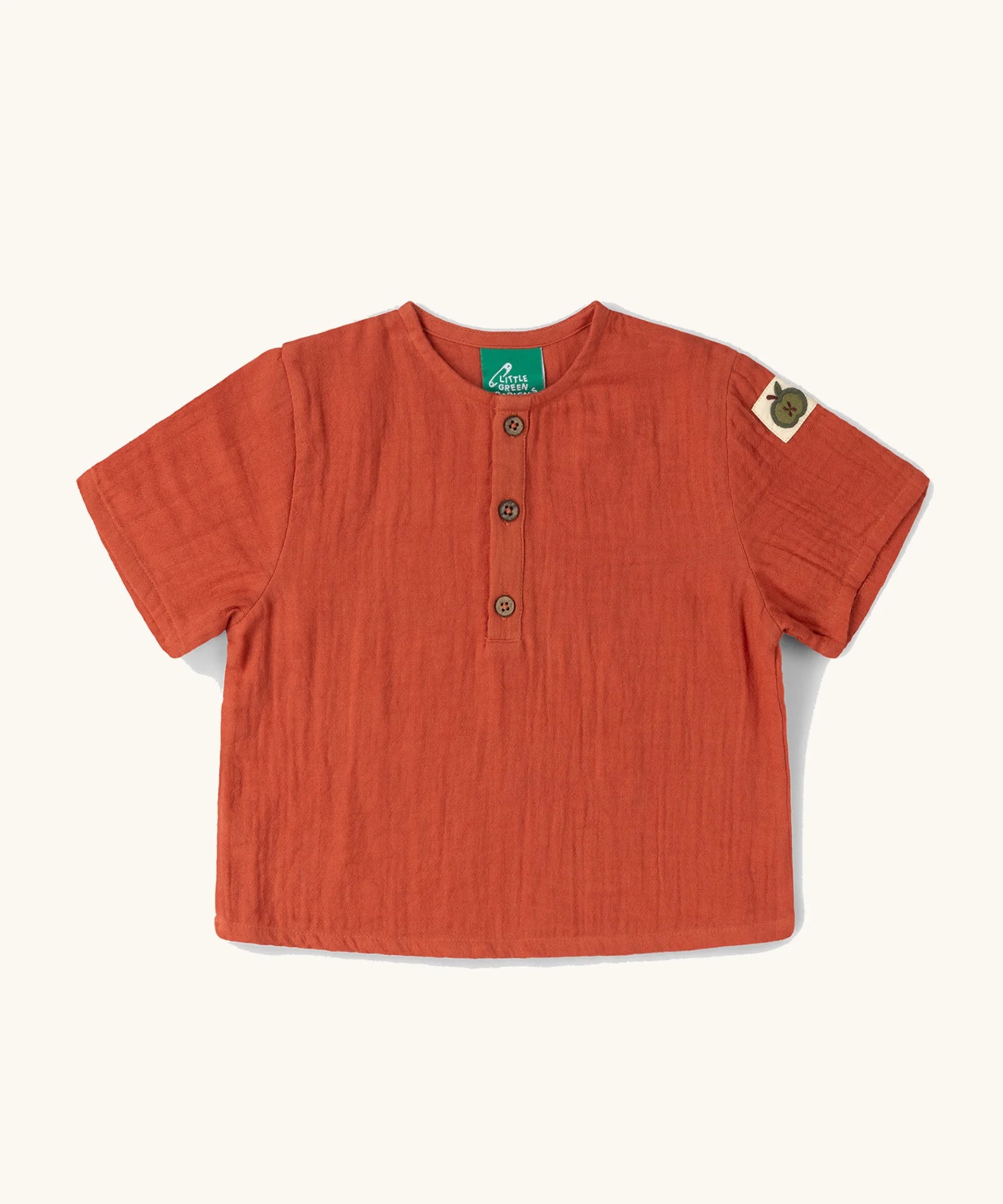 Little Green Radicals children's burnt ochre red short sleeved henley top with green apple tag on side of one arms and button up top.
