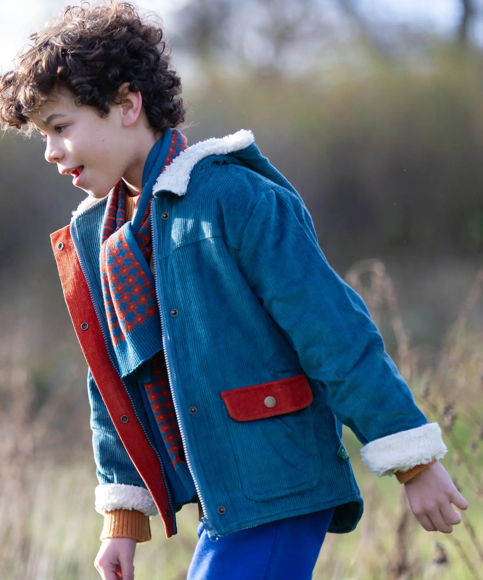 Child wearing a Little Green Radicals calm sea colourblock organic cotton sherpa lined toasty coat with scarf.