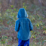 back of a child wearing a Little Green Radicals calm sea colourblock organic cotton sherpa lined toasty coat with hood up and blue trousers.