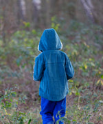 back of a child wearing a Little Green Radicals calm sea colourblock organic cotton sherpa lined toasty coat with hood up and blue trousers.