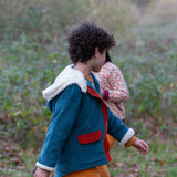 Side of a child wearing a Little Green Radicals calm sea colourblock organic cotton sherpa lined toasty coat with yellow gold trousers.