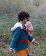 Side of a child wearing a Little Green Radicals calm sea colourblock organic cotton sherpa lined toasty coat with yellow gold trousers.
