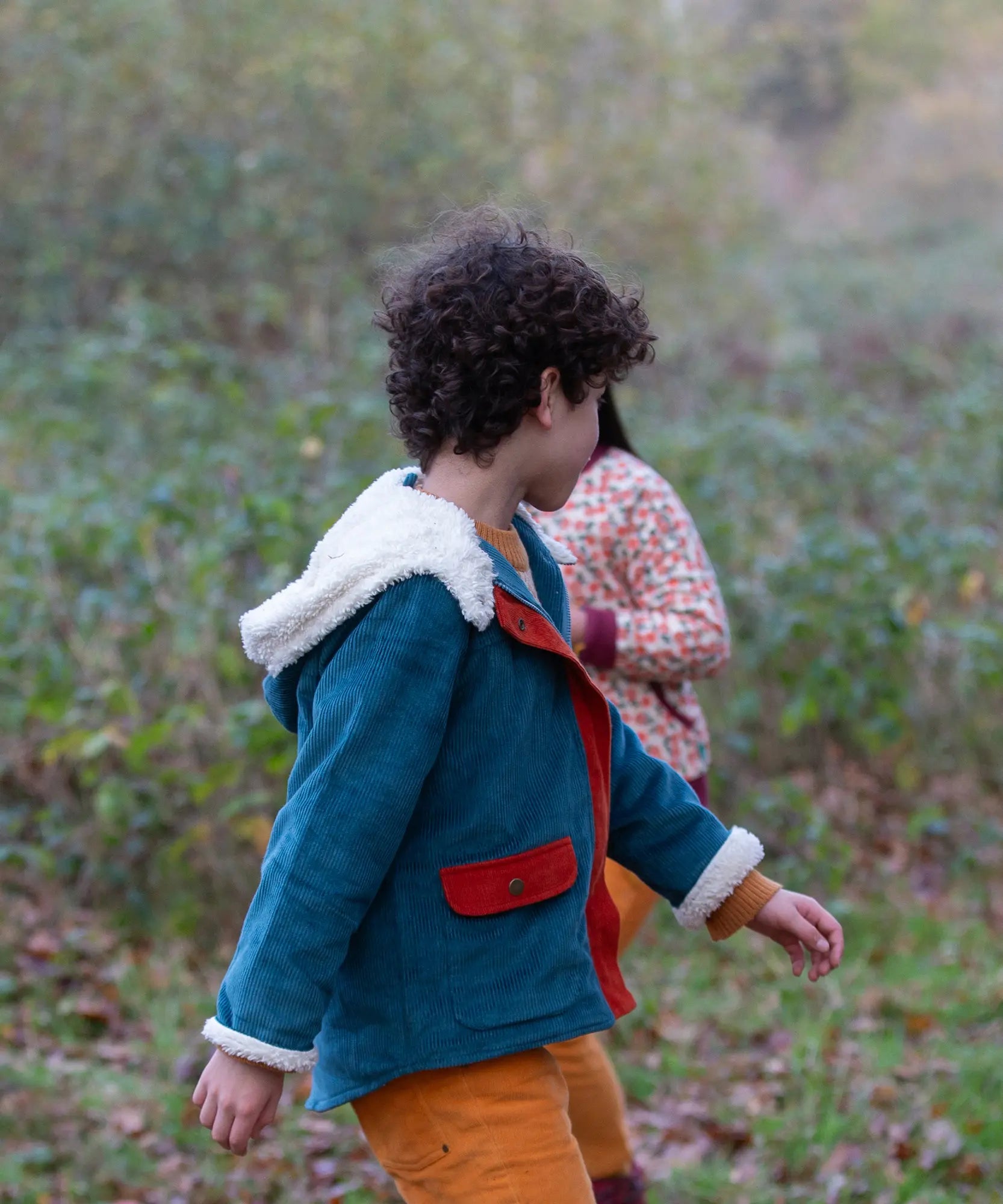Side of a child wearing a Little Green Radicals calm sea colourblock organic cotton sherpa lined toasty coat with yellow gold trousers.
