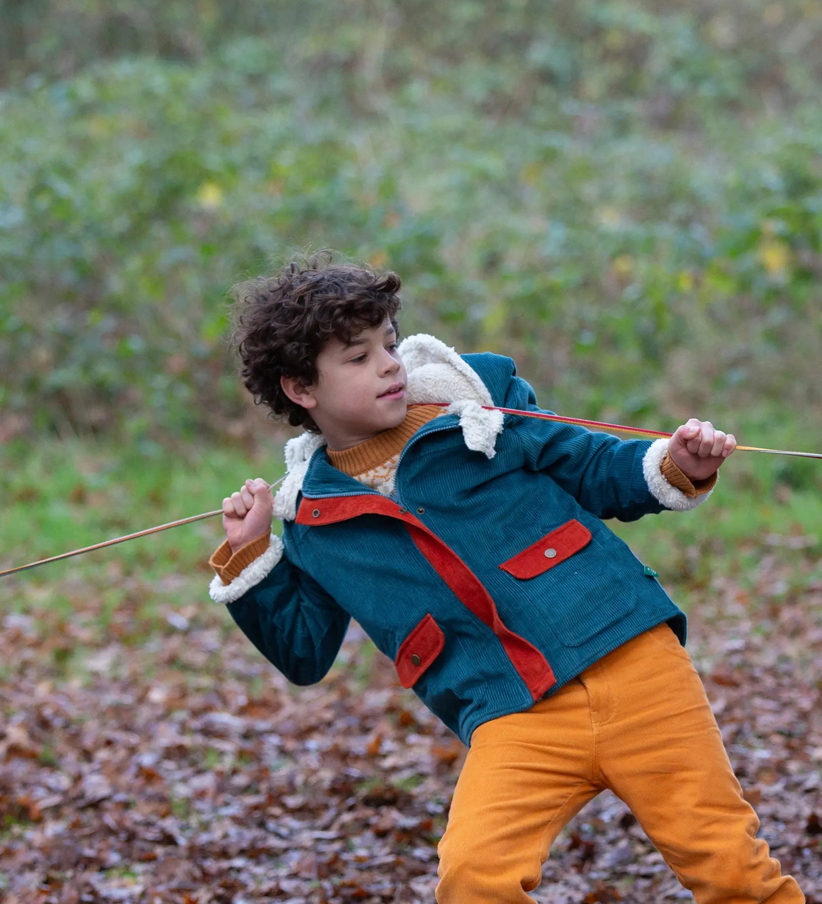 Child wearing a Little Green Radicals calm sea colourblock organic cotton sherpa lined toasty coat with yellow gold trousers.