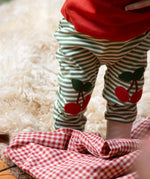 Close up of the red cherry knee appliques on the Little Green Radicals cherry knee patch green cream striped organic cotton joggers being worn with a red t-shirt.
