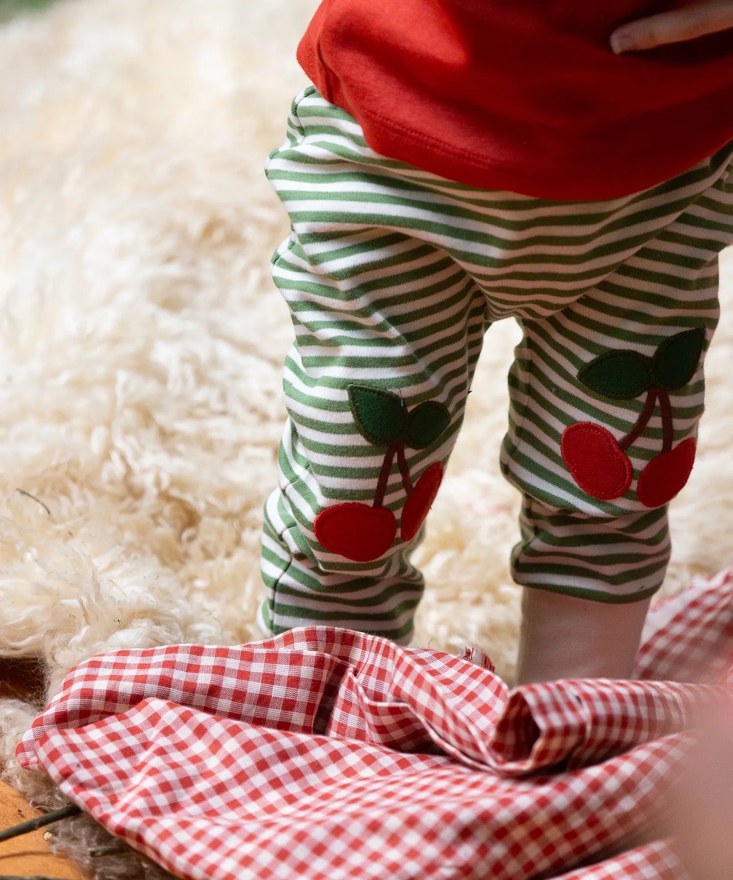 Close up of the red cherry knee appliques on the Little Green Radicals cherry knee patch green cream striped organic cotton joggers being worn with a red t-shirt.