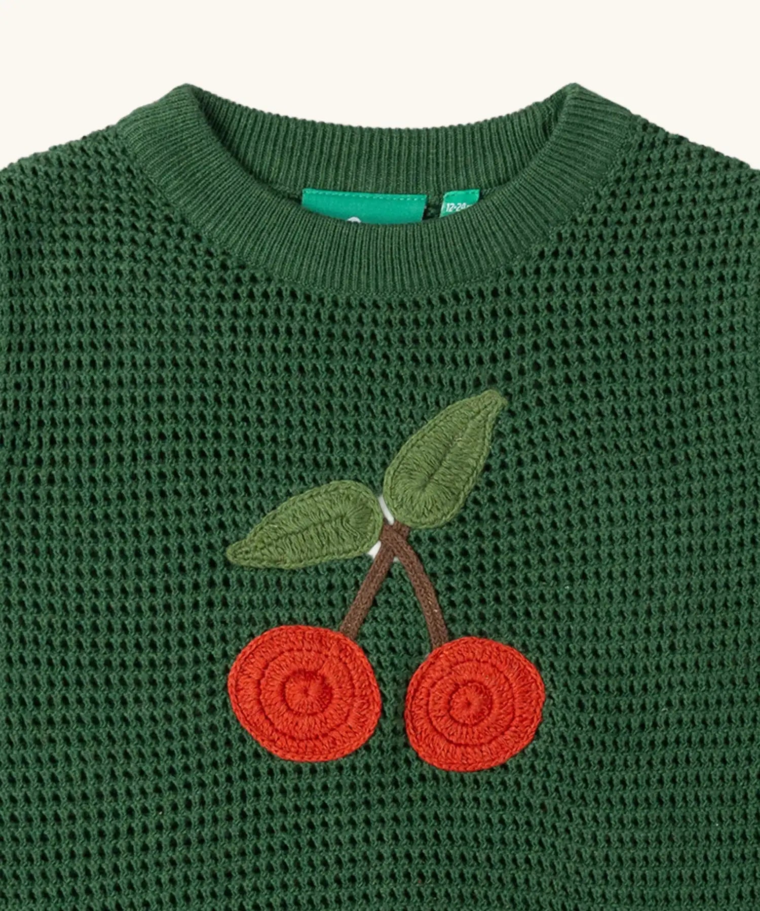 Close up of the cherry embroidered on the front of the Little Green Radicals kids dark green knitted sleeveless pullover.