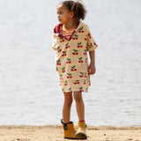 Little Green Radicals little cherries cream organic cotton kids hooded towel poncho on a child.The poncho has a popper closure on the neck and a kangaroo pocket on the front. 