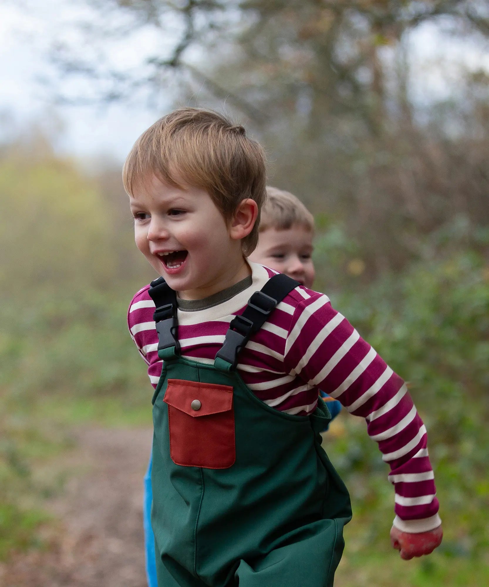 Child wearing the Little Green Radicals berry purple striped long sleeve top with green waterproof rain trousers. 