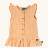 Little Green Radicals coral pink dropped waist children's dress with ochre yellow pom pom ribbon edging on the sleeves and collar.