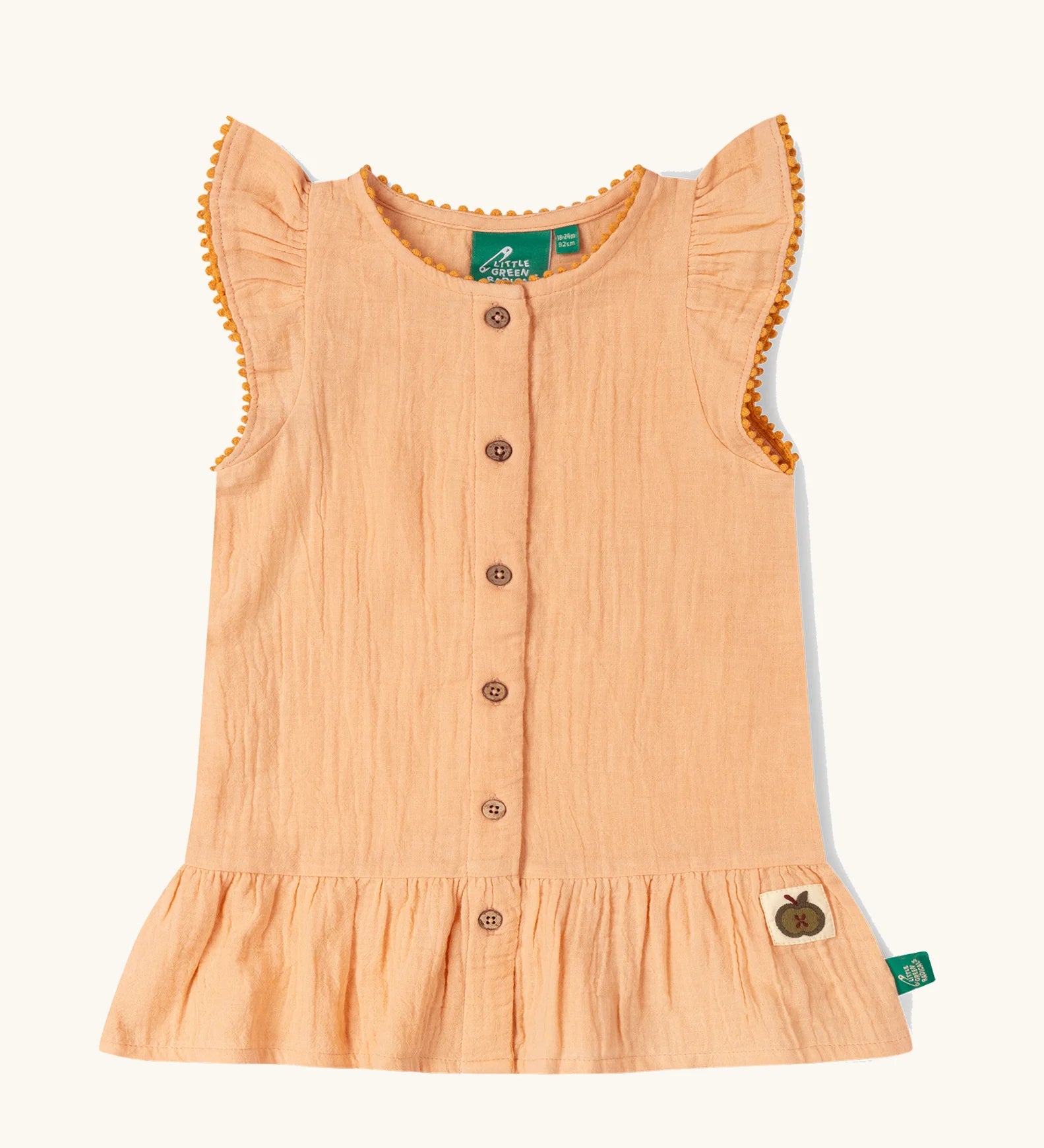 Little Green Radicals coral pink dropped waist children's dress with ochre yellow pom pom ribbon edging on the sleeves and collar.