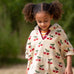 Child wearing the Little Green Radicals little cherries cream organic cotton kids hooded towel poncho.The poncho has a popper closure on the neck and a kangaroo pocket on the front. 