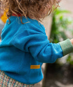 A view of the side of a child wearing the Little Green Radicals From One To Another Deep Blue Colour Block Knitted Cardigan. This organic cotton cardigan is part of a wide range of organic cotton, Fairtrade children's clothing and outerwear available here at Babipur.