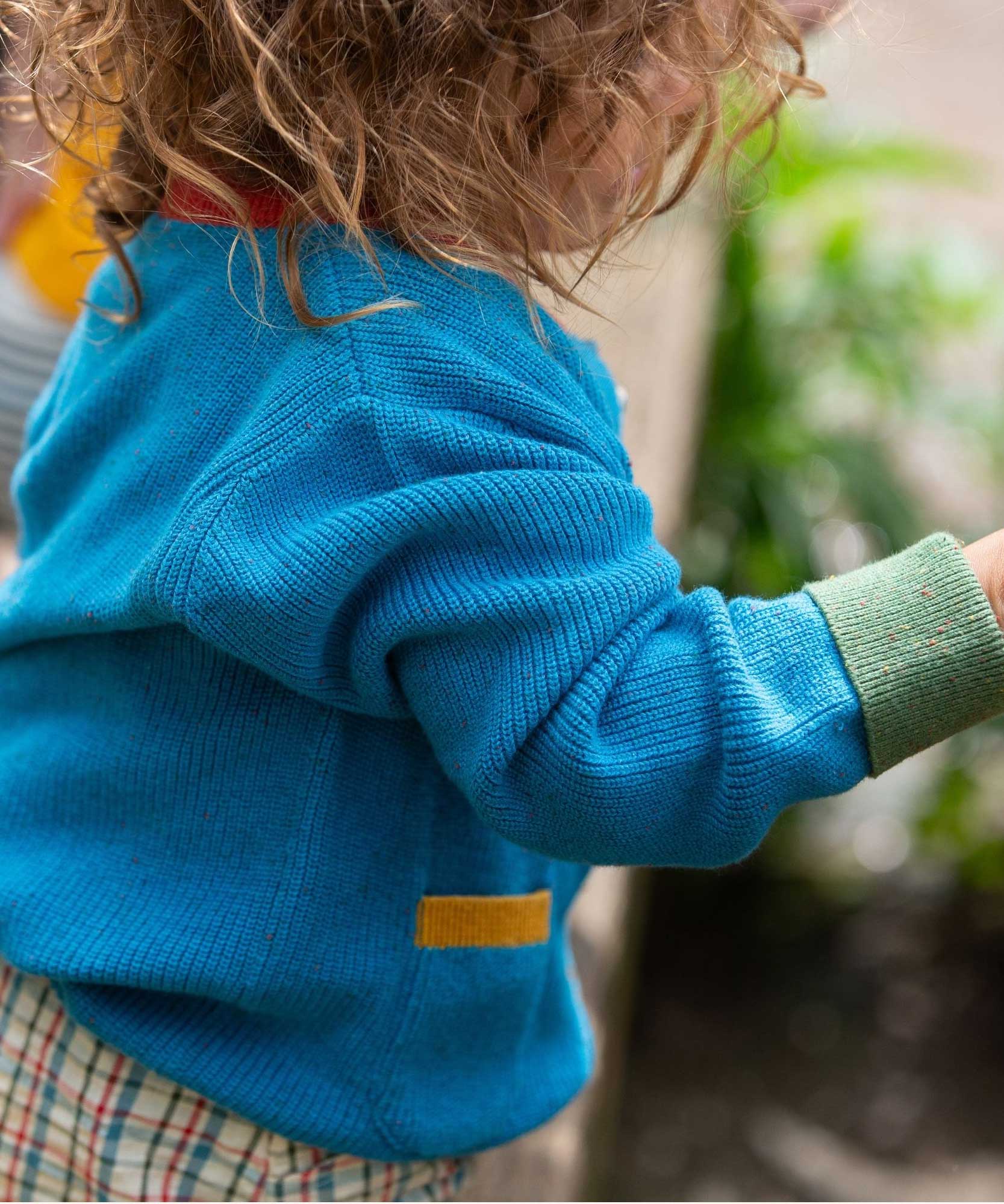 A view of the side of a child wearing the Little Green Radicals From One To Another Deep Blue Colour Block Knitted Cardigan. This organic cotton cardigan is part of a wide range of organic cotton, Fairtrade children's clothing and outerwear available here at Babipur.