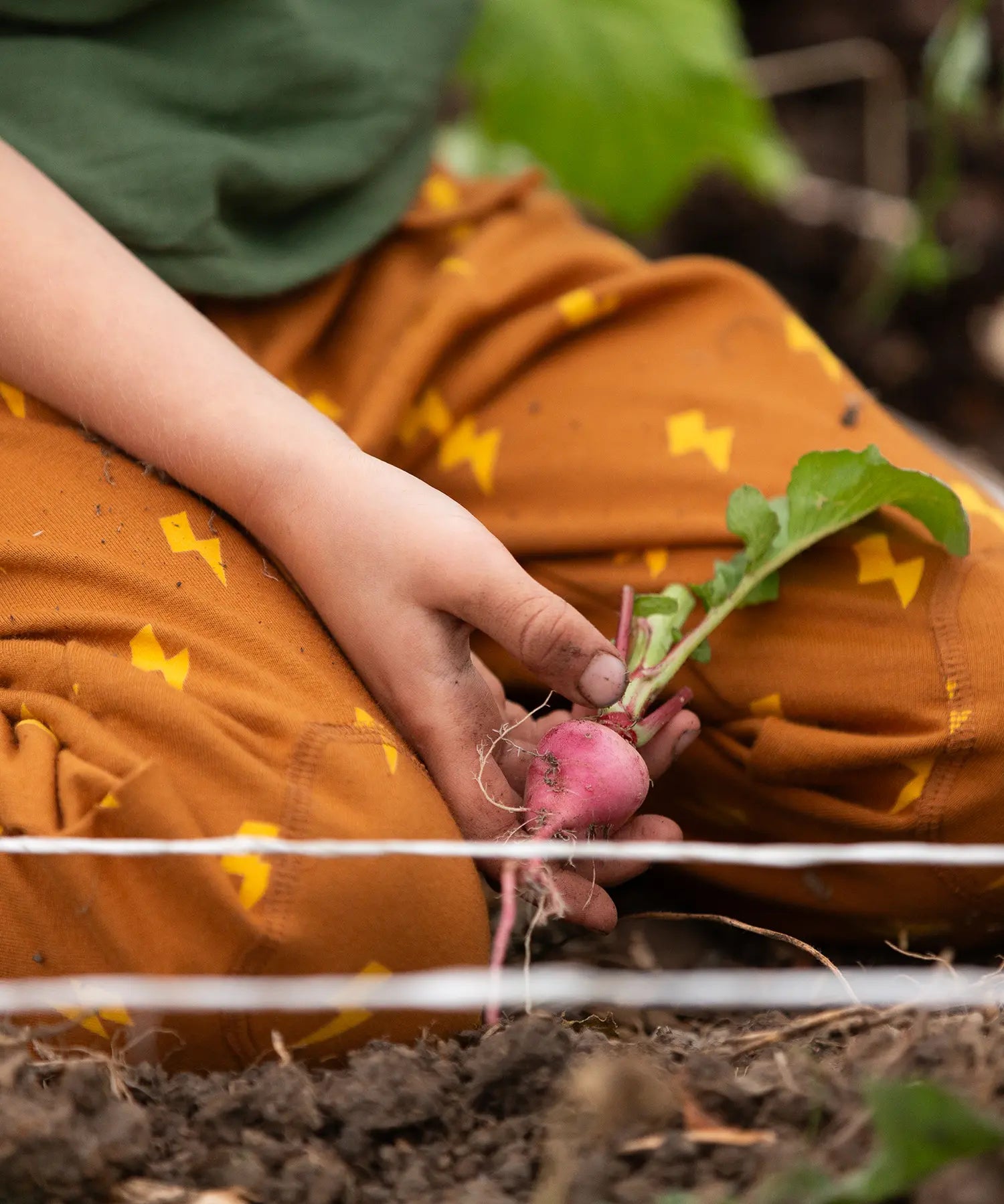 Close up of child kneeling down wearing the Little Green Radicals yellow gold repeat lightning print cosy organic cotton kids joggers with a green henley muslin t-shirt.