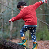 Child wearing Little Green Radicals organic cotton comfy joggers with a blue penguins design and a red knitted cardigan.
