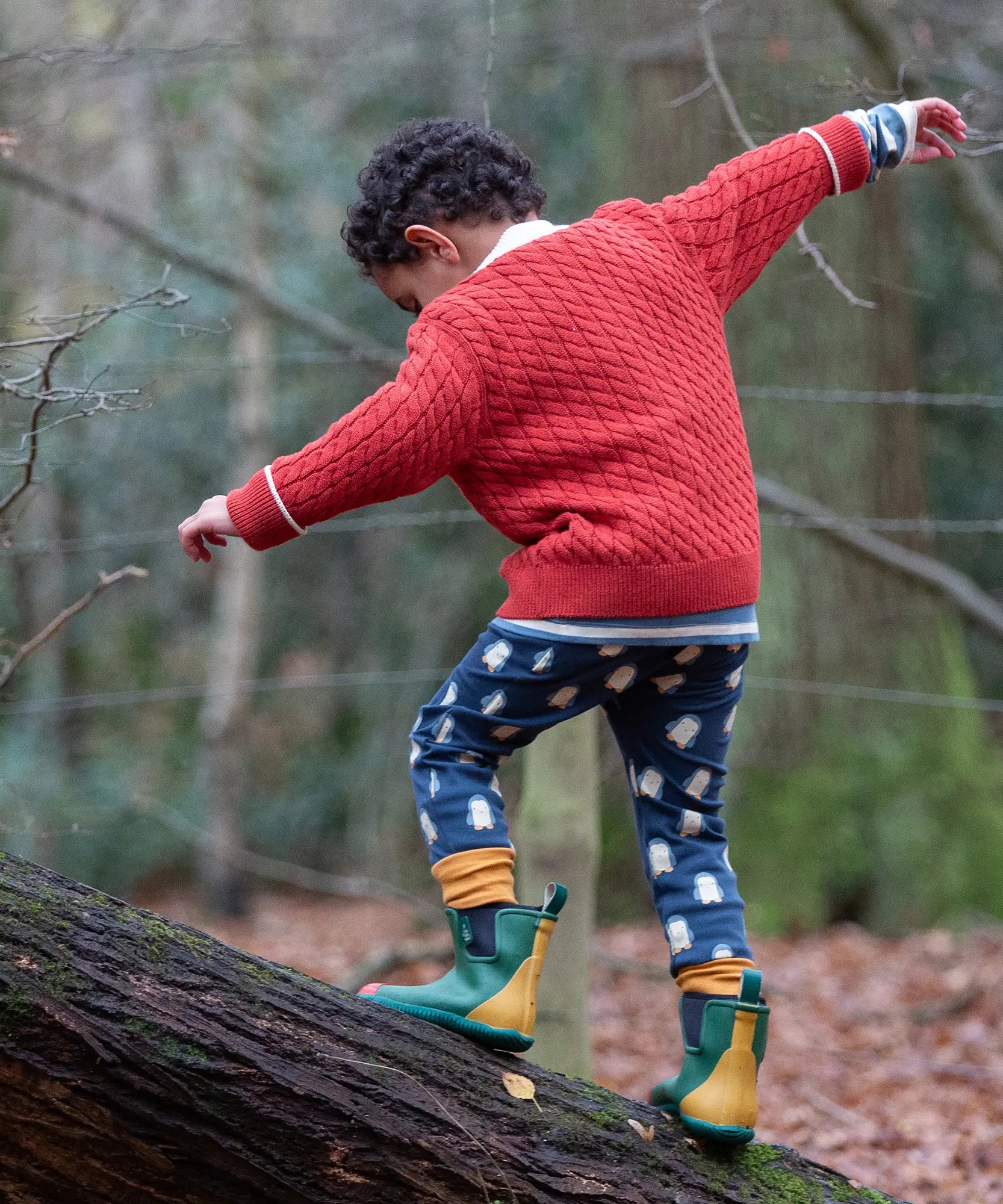 Child wearing Little Green Radicals organic cotton comfy joggers with a blue penguins design and a red knitted cardigan.