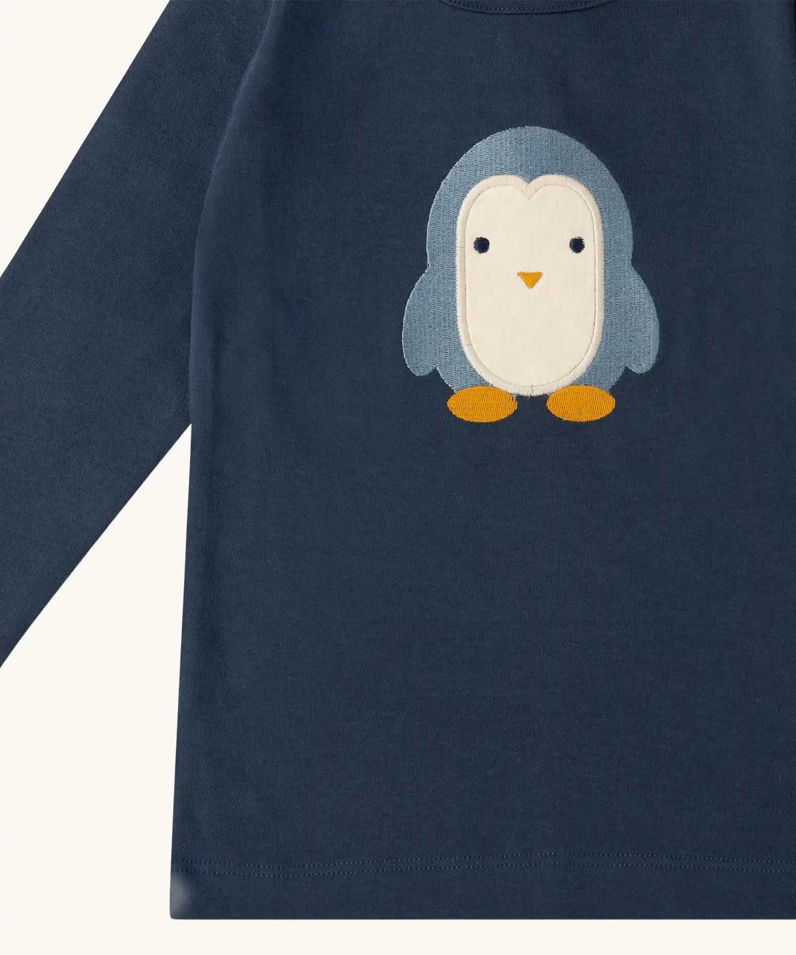 Close up of the Little Green Radicals blue penguins applique long sleeve organic cotton top in navy.