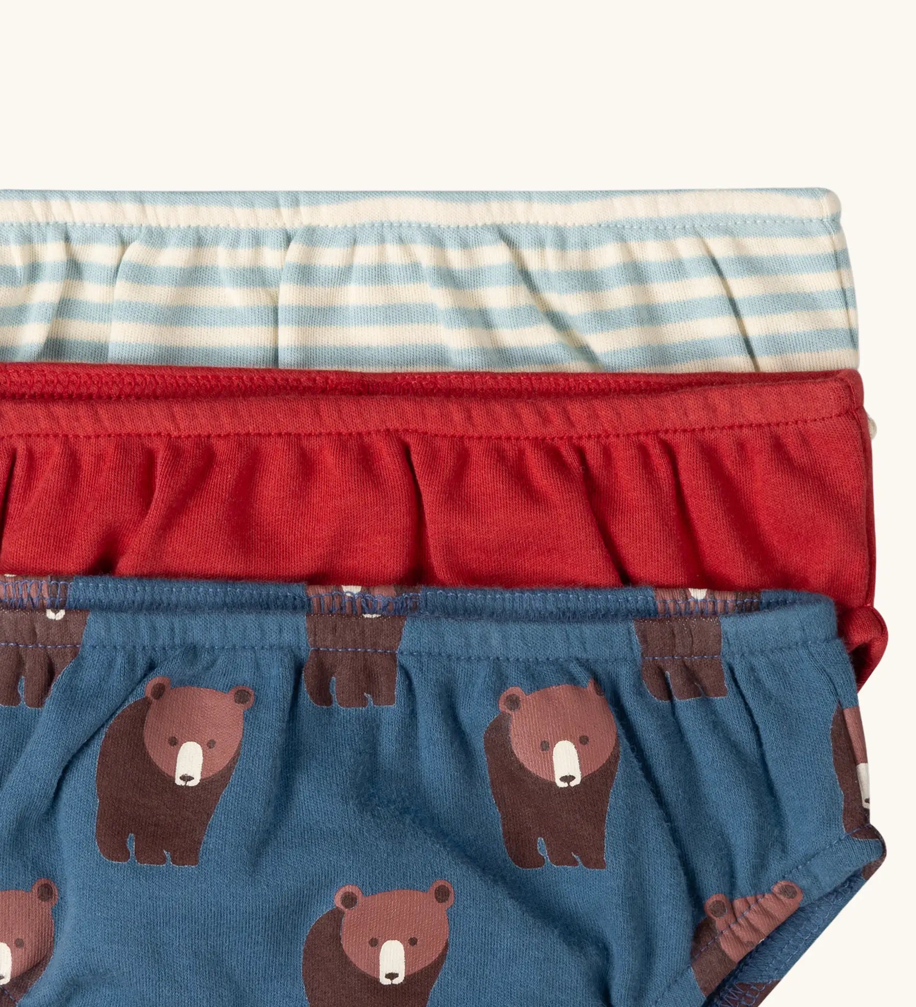 Close up of the elasticated waist on the Little Green Radicals children's organic cotton underwear 3 pack bears design. Brief style pants one navy with a brown bear print, one red and one blue and white stripes. 