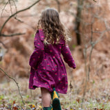 Back of a child wearing the Little Green Radicals pink flowers sailor dress in purple with green wellington boots. 