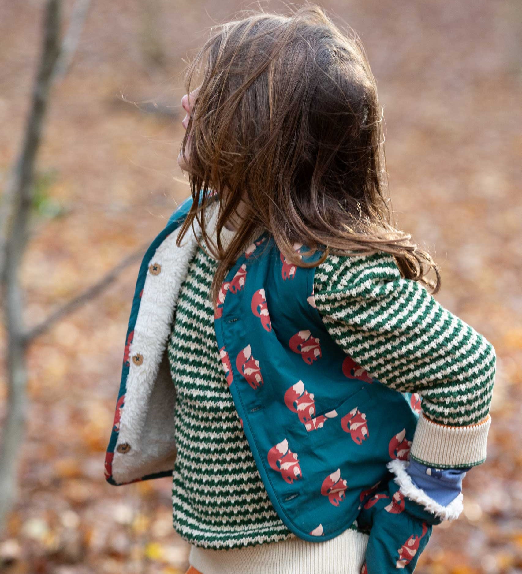 A child wearing the Little Green Radicals Children's Sherpa Fleece Gilet in the red foxes design. This gilet is a part of a wide range of organic cotton clothing for children available here at Babipur. 