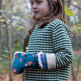 A child wearing the Little Green Radicals fox print sherpa fleece lined mittens with a olive green striped knitted jumper. The children's sized mittens are part of a wide range of organic cotton clothing for children available here at Babipur. 
