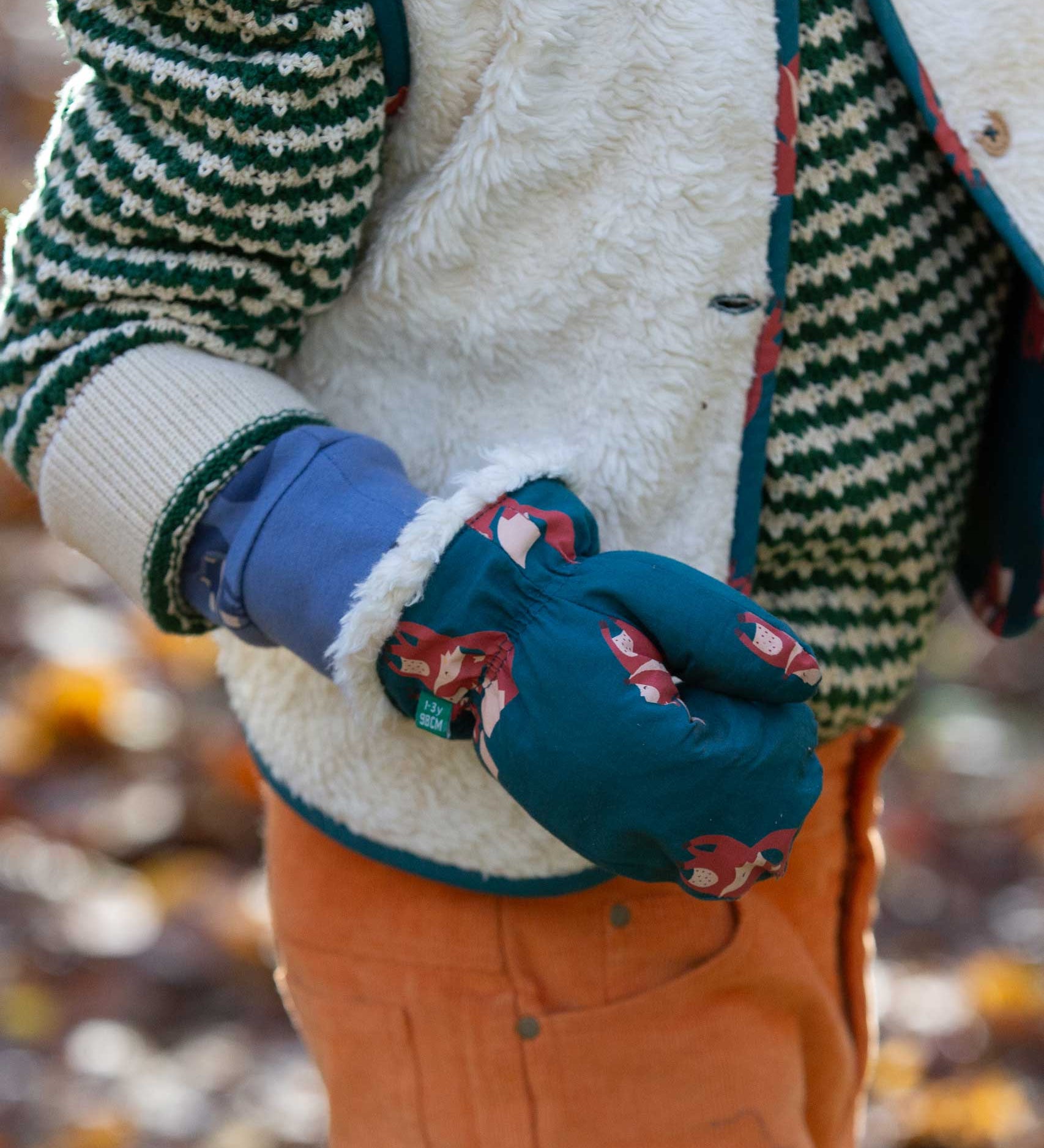 A close up of a child's hand, the child is wearing the Little Green Radicals fox print sherpa fleece lined mittens. The children's sized mittens are part of a wide range of organic cotton clothing for children available here at Babipur. 
