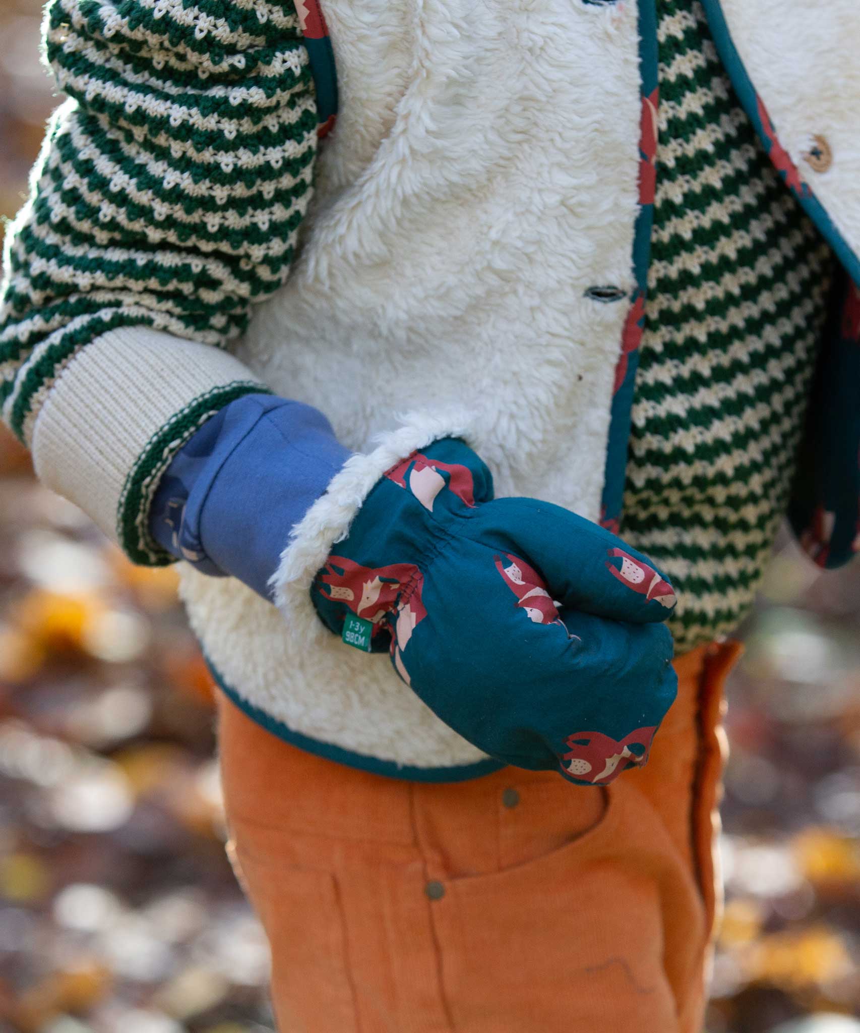A close up of a child's hand, the child is wearing the Little Green Radicals fox print sherpa fleece lined mittens. The children's sized mittens are part of a wide range of organic cotton clothing for children available here at Babipur. 
