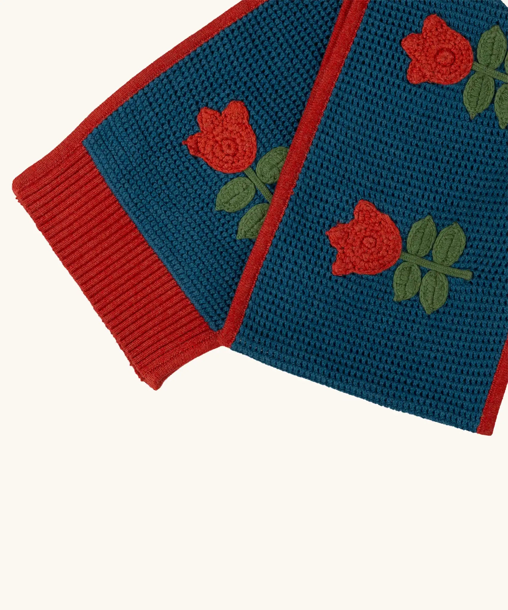 Close up of the Little Green Radicals tulips knitted blue scarf. Blue scarf with red tulips and red trim.