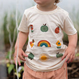Close up of the nature illustrations on the front of the Little Green Radicals cream vintage style kids organic cotton t-shirt being worn with peach shorts.