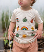 Close up of the nature illustrations on the front of the Little Green Radicals cream vintage style kids organic cotton t-shirt being worn with peach shorts.