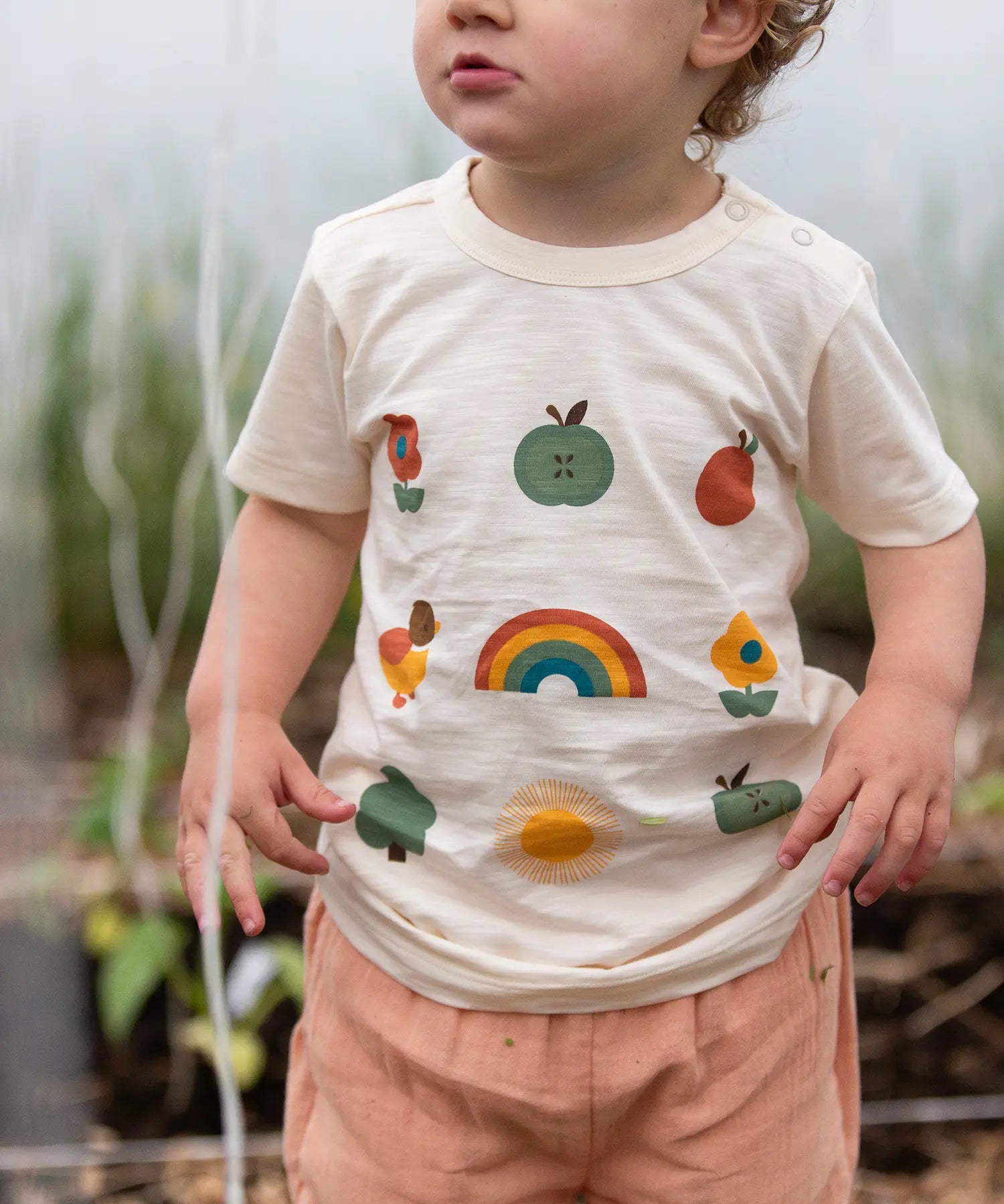 Close up of the nature illustrations on the front of the Little Green Radicals cream vintage style kids organic cotton t-shirt being worn with peach shorts.