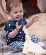 A baby wearing the Little Green Radicals  Full Moon T-Shirt & Jogger outfit set. The baby is sitting on a blanket with a cream coloured bunny comforter toy on their lap.  