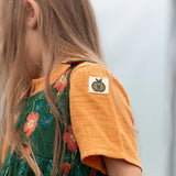 Close up of the green apple tage details on the side of the sleeve of the Little Green Radicals children's golden ochre yellow short sleeved henley top.