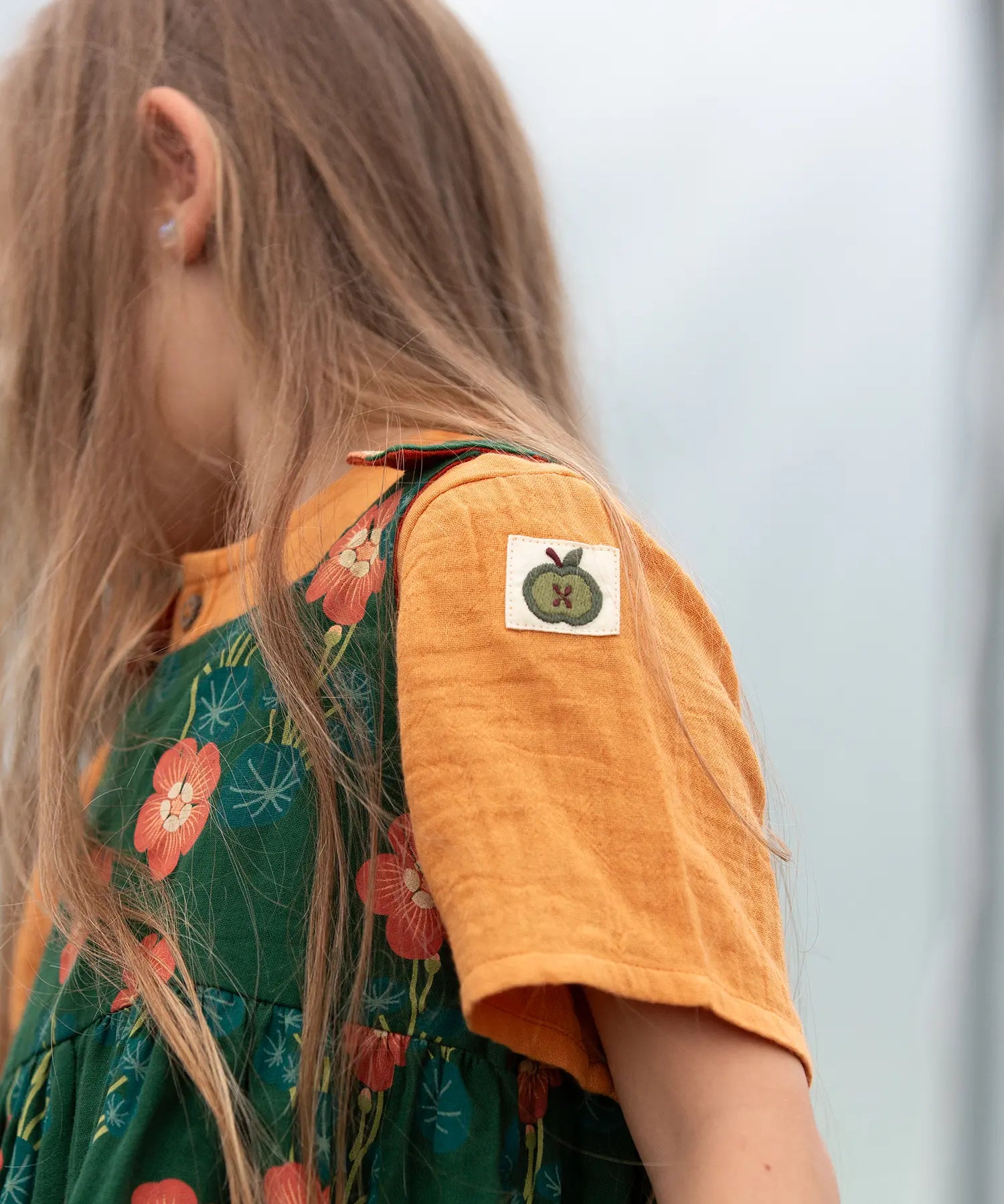 Close up of the green apple tage details on the side of the sleeve of the Little Green Radicals children's golden ochre yellow short sleeved henley top.