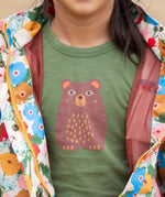 A close up of a child wearing the Little Green Radicals Kids Organic Cotton Green Bear Short Sleeve T-short.
