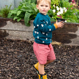 Child wearing the Little Green Radicals midnight moon print blue raglan organic-cotton children's sweatshirt with red pinstripe shorts and yellow wellington boots. 