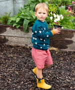 Child wearing the Little Green Radicals midnight moon print blue raglan organic-cotton children's sweatshirt with red pinstripe shorts and yellow wellington boots. 